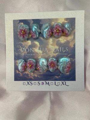 Opaline (M);ExtraShortAlmond  - Handgjorda press-on naglar med skimrande blå bas och detaljerade 3D-blommor i lila och rosa med gula detaljer. Naglarna har en extra kort almond form och är dekorerade med vita swirl-mönster för en unik look.M: 16 mm, 12 mm, 12,5 mm, 11,5 mm, 10 mm