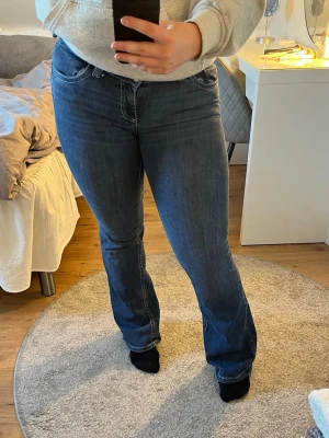 Blå bootcut jeans med vita sömmar - Säljer ett par blå bootcut jeans med snygga vita kontrastsömmar och klassiska fem fickor. Jeansen har låg midja och utsvängda ben. Materialet är denim med lätt stretch. Använda ett par fåtal gånger, inte slitna alls nertill 