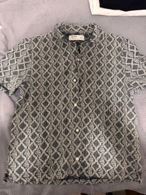 Mönstrad kortärmad skjorta Hollister - Säljer en svartvit kortärmad skjorta från Hollister i boxy fit. Skjortan har ett grafiskt mönster, knappar framtill och en avslappnad passform. Perfekt för dig som gillar en unik och trendig stil.