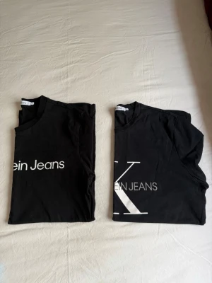 Calvin Klein Jeans t-shirts, storlek M - Två svarta t-shirts från Calvin Klein Jeans med tryck framtill. Båda t-shirtarna är i storlek M. Förvarad i djur- och rökfritt hem, knappt använd. De säljes tillsammans. 