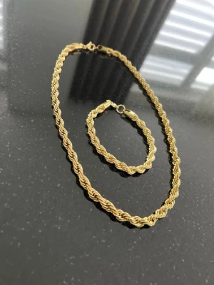 Cordell Set - Säljer ett snyggt guldfärgat halsband med armband med tvinnad kedja. Halsbandet & armbandet har en klassisk design med flätad struktur som ger en cool och trendig look. Perfekt accessoar för att lyfta din outfit med lite extra bling.