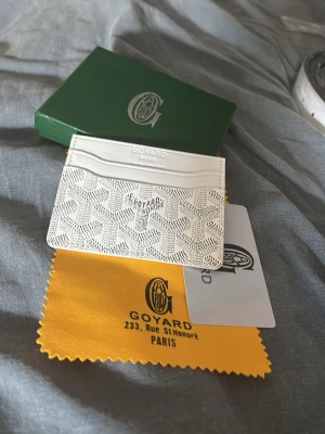 Vit kortfodral goy - Snyggt vitt kortfodral med klassiskt mönster och flera kortfack. Tillverkad med tryckt logotyp på framsidan. Kommer med o ask och putsduk, perfekt för dig som vill ha något stilrent och lyxigt i fickan.