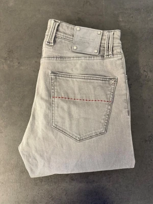 Tramarossa Leonardo, stl 31  - Snygga ljusgrå jeans i rak modell med klassisk femficksdesign. Jeansen har en diskret röd söm på bakfickan och silverfärgade nitar vid linningen. Tillverkade i mjukt denimtyg som ger en avslappnad look.