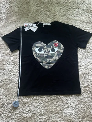 Svart Comme des Garcons play t shirt med stort camouflage hjärta - Svart Comme des Garcons play t shirt med stort camouflage hjärta i mitten!💚