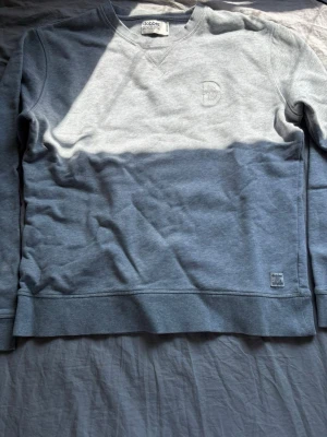 Grå sweatshirt från Dobber - Klassisk grå sweatshirt från Dobber med rund halsringning och ribbade muddar vid ärmslut och nederkant. Diskret broderad Dobber-logga på bröstet och liten etikett nertill. Perfekt för en avslappnad stil.
