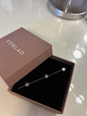Silverarmband med stjärnor från Edblad - Snyggt och stilrent armband i silverfärg från Edblad. Armbandet har en tunn kedja och är dekorerat med flera små stjärnor i metall. Jättebra skick, säljer för att jag använder guld smycken nu.
