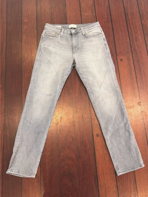 Grå jeans - Säljer ett par helt nya ljusgrå jeans med rak passform och klassisk femficksdesign. Jeansen har normal midja och är tillverkade i ett mjukt denimtyg. Perfekta för en avslappnad och trendig look.