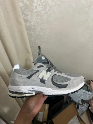 Grå New Balance 2002R sneakers - Snygga New Balance 2002R sneakers i grått med mesh och mocka på ovandelen. Skon har vita och mörkgrå detaljer, samt en vit och svart sula med N-ergy dämpning. Klassisk N-logga på sidan och reflekterande detaljer. Perfekt för dig som gillar streetwear och sportig stil.