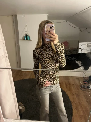 Leopardmönstrad långärmad topp - Säljer en slim leopardmönstrad långärmad topp med hög hals. Toppen har en beige och svart färgskala och är tillverkad i ett stretchigt syntetmaterial som sitter tight mot kroppen. Perfekt för dig som vill sticka ut med ett djurmönster.