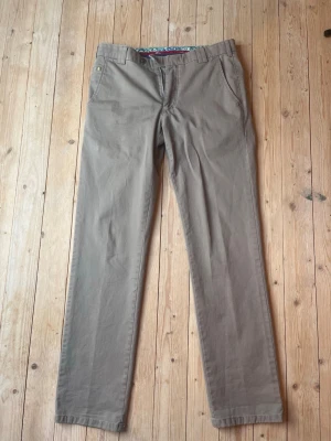 Beige chinos med raka ben - Snygga beige chinos med raka ben och klassisk passform. Byxorna har sidofickor fram och två bakfickor med knapp. Perfekta för en avslappnad men stilren look. Passar perfekt med allt från t-shirt till kavaj! 