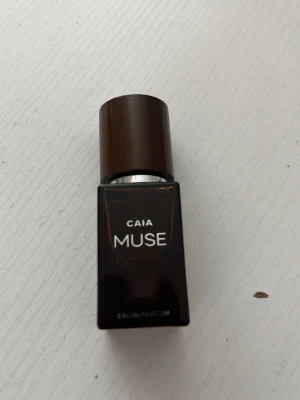 CAIA Muse Eau de Parfum - Snygg parfymflaska från CAIA i modellen Muse. Flaskan är rektangulär och gjord av mörkbrunt glas med ett matchande brunt lock. Texten på flaskan är vit och designen känns modern och stilren. Perfekt för dig som gillar exklusiva dofter.