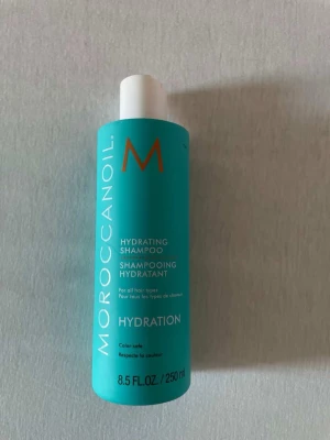 Moroccanoil Hydrating Shampoo - Säljer en Moroccanoil Hydrating Shampoo i en turkos plastflaska med vitt lock. Schampot är återfuktande och passar alla hårtyper. Flaskan rymmer 250 ml och har tydlig text i vitt och orange. Perfekt för dig som vill ha mjukt och återfuktat hår.