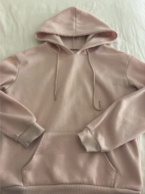 Ljusrosa hoodie med ficka - En stilren ljusrosa hoodie med huva och dragsnören. Hoodien har en stor magficka framtill och ribbade muddar vid ärmar och nederkant. Tillverkad i mjukt sweatshirtmaterial som är perfekt för en avslappnad look.