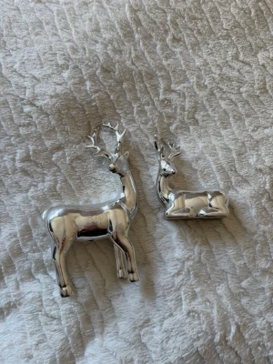 Två silverfärgade renfigurer i metall - Säljer två stilrena renfigurer i blank silverfärgad metall. Den ena renen står upp och den andra ligger ner. Perfekta som dekoration till vinter eller jul. Ger ett modernt och elegant intryck i hemmet.