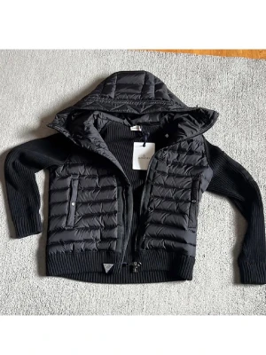 Svart cardiganjacka från Moncler med NFC SCAN - Svart cardiganjacka från Moncler med stickade ärmar och quiltad front. Jackan har huva, dragkedja och ribbade muddar. Perfekt för lager-på-lager och snygg streetstil. PRIS KAN DISKUTERAS VID SNABB AFFÄR