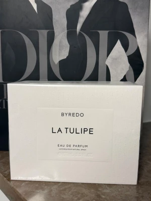 Byredo La Tulipe Eau de Parfum - Byredo La Tulipe Eau de Parfum är en elegant parfym i en stilren vit kartong med subtilt mönster. Doften kommer i sprayformat och förpackningen har minimalistisk design med svart text på vit bakgrund. Perfekt för dig som gillar exklusiva och moderna dofter.