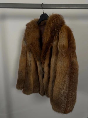 Äkta pälsjacka - Äkta vintage pälsjacka i äkta rävpäls. Långhårig och fyllig struktur med mjuk underull och glansiga täckhår. Modellen är rak med lätt vidd, bred sjalkrage och knäppning framtill med hyskor/hooks. Helfodrad med brunt satinliknande foder. Uppskattas passa S–M beroende på önskad passform. Bra skick på pälsen. Fodret är lagat vid armhålorna.
