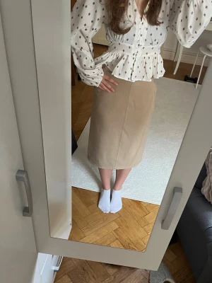 Beige pennkjol - Stilren beige pennkjol i mjukt material. Kjolen har en klassisk midilängd, raka linjer och diskreta fickor framtill. Perfekt att matcha med en blus eller stickad tröja för en snygg look.