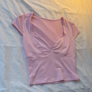 Ljusrosa topp med spetsdetalj - Söt ljusrosa topp med korta ärmar och v-ringning. Toppen har en spetsdetalj längs urringningen. Perfekt nu mot våren/sommaren. 💞SKRIV FÖR FRAKTEN. Helt ny oanvänd