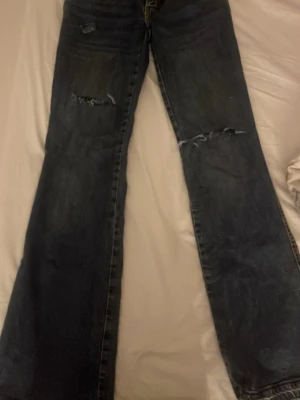 Mörkblå slitna bootcut jeans - Säljer ett par mörkblå bootcut jeans med slitningar och hål på låren och knäna. har gjort hålen själv köpte jeansen för 400 på lager de är i full lenght 