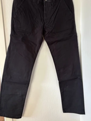 Svarta chinos med raka ben - Snygga svarta chinos med raka ben och klassisk passform. Byxorna har sidofickor fram och två bakfickor med knapp. Tillverkade i mjukt bomullstyg som ger en skön känsla och stilren look. Perfekta för dig som vill ha en clean och enkel stil. Storlek 31x32