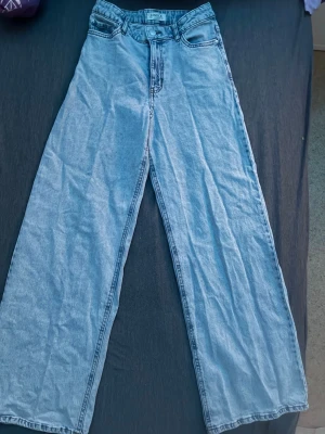 Ljusblåa baggy high waist jeans från Gina Lindex  - Säljer ett par ljusblåa wide leg jeans från Lindex. Jeansen har hög midja, klassiska fyra fickor. Tillverkade i denim med bälteshällor och knappgylf. Perfekta för en avslappnad och trendig look.