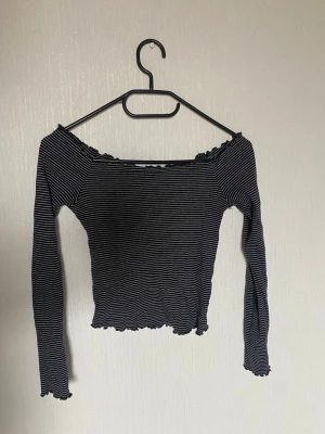 Randig offshoulder topp - Trendig svart offshoulder topp med tunna vita ränder. Toppen är ribbad och har långa ärmar. 