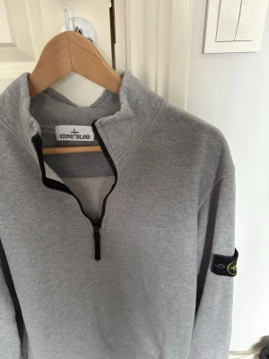 Grå half-zip sweatshirt Stone Island - Grå sweatshirt med half-zip och hög krage från Stone Island. Tillverkad i mjukt bomullsmaterial. Perfekt för en avslappnad och stilren look.