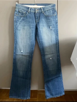 Blå jeans med slitningar - Snygga blå jeans med slitningar framtill och ljus tvätt. Klassisk femficksmodell med broderade detaljer i gult på bakfickorna. Tillverkade i denim med en avslappnad passform och låg midja. Perfekta för en trendig och avslappnad stil.