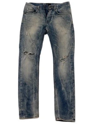 Blå slitna Tiger of Sweden jeans med hål - Ett par blå jeans med slitningar och hål på båda benen. Jeansen har klassisk femficksdesign, rak passform och tydlig tvättad look. Perfekta för en avslappnad och cool stil. Passar bra med både boots och moderna sneaker silhuetter. Materialet är denim i bomull.