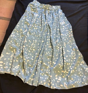 Blå långkjol med vita prickar - Säljer en blå långkjol med vitt prickigt mönster. Kjolen har resår i midjan för skön passform och är gjord i ett mjukt, lätt tyg som faller snyggt. Perfekt för dig som gillar en avslappnad men ändå stilren look.