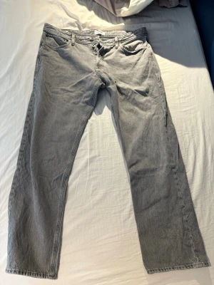 Grå raka jeans med knappgylf - Säljer ett par grå jeans med rak passform och knappgylf. Jeansen har klassiska fem fickor och är tillverkade i denim. Perfekta för dig som gillar en enkel och stilren look. W36 L32