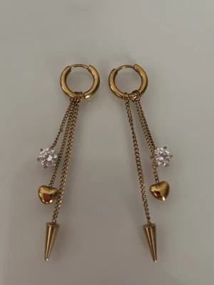 Peak Hoops Multi Heart Gold örhängen - Snygga guldfärgade örhängen från Edblad med ringformad bas, hängande kedjor, små hjärtan, spetsiga detaljer och gnistrande stenar. Nästintill oanvända, i nyskick.