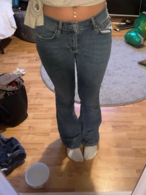 Blå bootcut jeans med låg midja - Säljer ett par blå bootcut jeans med låg midja och klassiska fem fickor. Jeansen har en avslappnad passform och är perfekta för en trendig och avslappnad stil. Materialet är denim i bomull och de har snygga söm-detaljer.