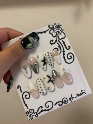 Press-on naglar med silverdetaljer - Snygga press-on naglar i mandelform med vit, nude och silver design. Naglarna har coola stjärndekorationer, silvriga pärlor och metallicdetaljer för en trendig look. Perfekt för dig som vill ha unika och kreativa naglar utan att gå till salong.