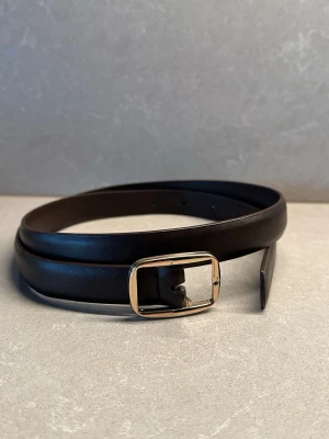 Mörkbrunt skärp  - Stilrent mörkbrunt skärp med guldfärgat spänne. En snygg detalj som lyfter vilken outfit som helst – perfekt till jeans, kostymbyxor eller klänning.  I mycket fint skick. Klassisk modell som passar både vardag och fest.  Bältets bredd: 1,8cm  Köpt från vinted men var för liten och säljer den därför på nytt