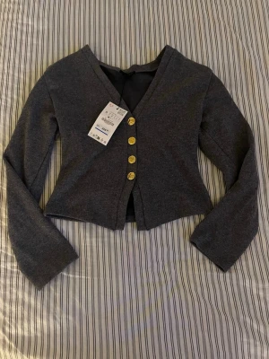 Mörkgrå cropped kofta med guldknappar - Snygg mörkgrå cropped topp från ZARA med guldknappar.  Materialet känns mjukt och stretchigt. Har fortfarande prislappen och ej använts.