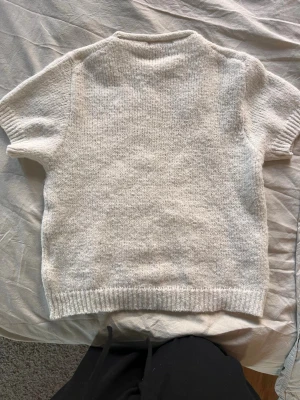 Beige stickad t-shirt med kort ärm - En enkel och stilren beige stickad t-shirt med korta ärmar och ribbstickade muddar vid ärmslut och nederkant. Perfekt för lager-på-lager och passar till det mesta. Mjuk och skön känsla i materialet.