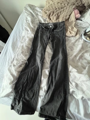 Svarta bootcut jeans med fickdetaljer💕 strl 158!💕 - Säljer ett par svarta bootcut jeans med snygga fickdetaljer fram och bak. Jeansen har låg midja och vida ben, vilket ger en retro vibe. Materialet är klassisk denim och de har dekorativa sömmar på fickorna. Perfekta för dig som gillar en avslappnad men trendig stil.Passar till allt!💕💕