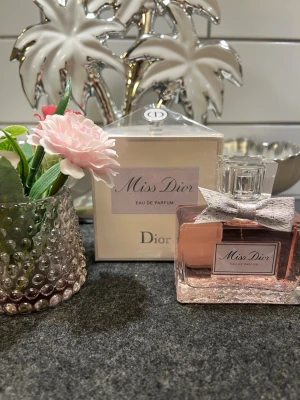 Miss Dior Eau de Parfum 100ml - Miss Dior Eau de Parfum från Dior i en elegant glasflaska med rosa doftvätska och en söt silverfärgad rosett vid halsen. Kommer i originalförpackning 100ml helt ny