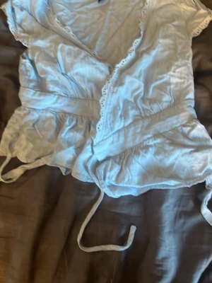 Ljusblå omlottopp med spets från SHEIN - Supersöt ljusblå omlottopp från SHEIN med knytband i midjan och fina spetsdetaljer längs kanterna. Toppen har korta ärmar och volang nertill, perfekt för en chill och trendig look.