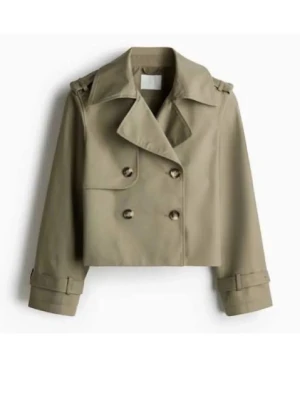Kort grön trenchcoat med dubbelknäppning - Stilren kort trenchcoat i beige med dubbelknäppning och bred krage. Jackan har axelklaffar, justerbara ärmslut och en boxig passform. Tillverkad i ett slätt tyg som ger en klassisk look. Perfekt för dig som vill ha en modern twist på trenchcoaten.