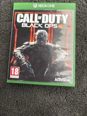 Call of Duty Black Ops III Xbox One - Säljer Call of Duty Black Ops III till Xbox One. Spelet kommer i ett grönt plastfodral med omslag och skiva, samt Season Pass-häfte. Omslaget har en futuristisk soldat i svart och orange. Märkt med 18+ PEGI och utvecklat av Treyarch.