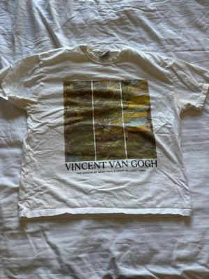 Vit Van Gogh t-shirt med tryck - Snygg vit t-shirt med konstnärligt tryck av Vincent Van Gogh på framsidan. Motivet föreställer 'The Garden of Saint Paul's Hospital' och texten är tryckt under bilden. Klassisk passform och rund hals, perfekt för dig som gillar konst och stilrena plagg.
