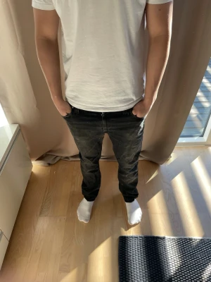 Svarta slim fit jeans - Säljer ett par svarta slim fit jeans med klassisk femficksdesign och lätt slitna detaljer. Jeansen har raka ben och normal midja, perfekt för dig som gillar en stilren look. Materialet är denim och färgen är mörkgrå/svart.