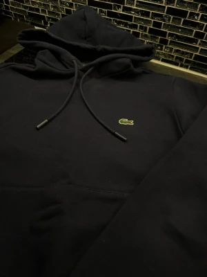 Lacoste hoodie  - Säljer en mörkblå hoodie från Lacoste med klassisk krokodillogo på bröstet. Perfekt för dig som gillar stilren design och ikoniska märken.