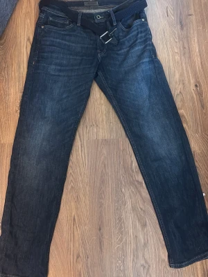 Mörkblå jeans från Jack & Jones - Säljer ett par mörkblå jeans från Jack & Jones med klassisk femficksdesign och raka ben. Jeansen har snygga slitningar och är tillverkade i denim. Perfekt för dig som gillar en stilren look.
