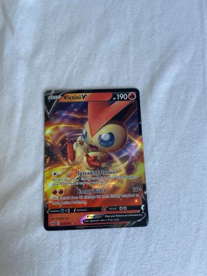Pokémonkort Victini V 190 HP - Säljer ett Victini V Pokémonkort med 190 HP. Kortet har färgstark design med Victini i centrum och coola effekter i bakgrunden. Det är en V-kortvariant med attacker som Spreading Flames och Energy Burst. Perfekt för samlare eller Pokémonspelare.