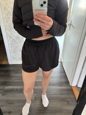 Svarta sportiga shorts med resår - Svarta shorts med elastisk midja och dragsko. Modellen är lös och har rundade benslut för en sportig look. Perfekta för träning eller chill. Materialet känns lätt och bekvämt mot huden. OBS! Inga undershorts, det är ett par andra jag har under. 