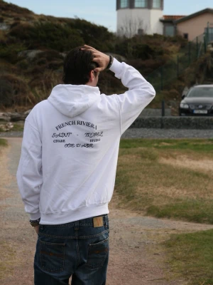 Vit hoodie från Civare (French riviera collection) - Vit hoodie med tryck i marinblått på ryggen där det står 'French Riviera', 'Saint-Tropez' och 'Côte d'Azur'. På bröstet finns en liten Civare-logga. Hoodien har huva och känguruficka. Perfekt för en chill och stilren look.